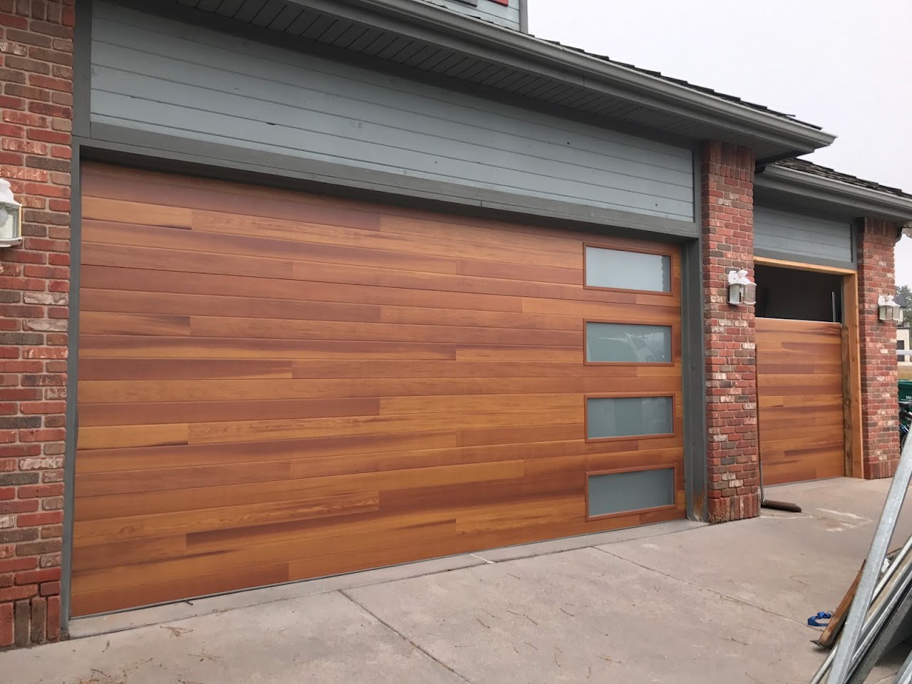 Modern horizontal wood-slat garage door with frosted glass panels on a brick home